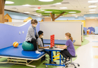 Brightly colored physical and occupational therapy space with two therapists place a game with a teenage boy