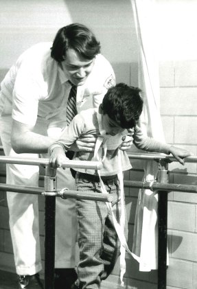 A boy assisted in walking by a doctor