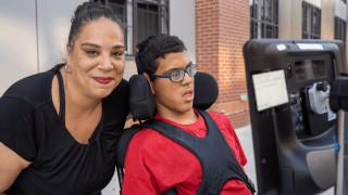 A smiling mother with her teenage son in a wheelchair on a New York sidewalk