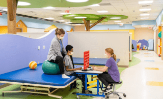 Brightly colored physical and occupational therapy space with two therapists place a game with a teenage boy