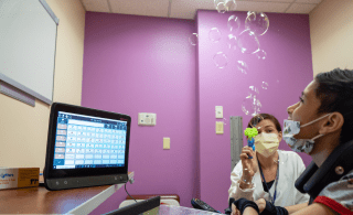 Child working on speech with bubbles and assistive communication device