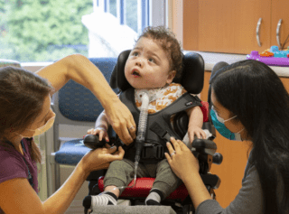 young child in adaptive stroller with mother and occupational therapist