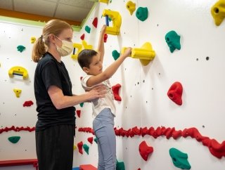 child on a climbing wall with help of therapist