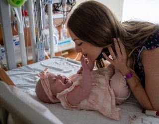 infant in hospital crib playing with mom