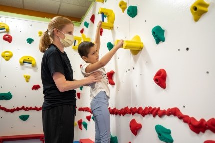 A girl using a climbing wall with a therapist's help