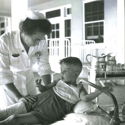 Boy in cast cared for by nurse in white dress