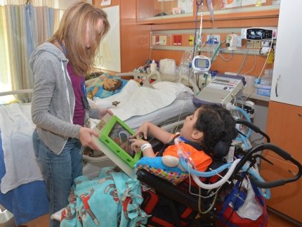 Boy in a wheelchair using an adaptive communication device with a speech therapist