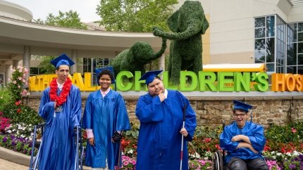 four graduates in front of blythedale children's hospital sign