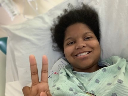 child in bed giving peace sign