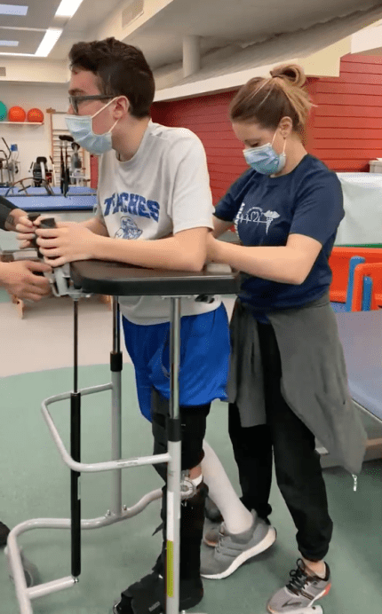teen boy using a walker assisted by a therapist