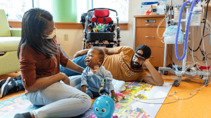 A baby plays on the floor of his hospital room with his mom and dad